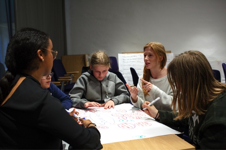 Teenagers sitting around a table talking and brainstorming on a poster sheet