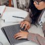 Student writing on a laptop with notes and a textbook