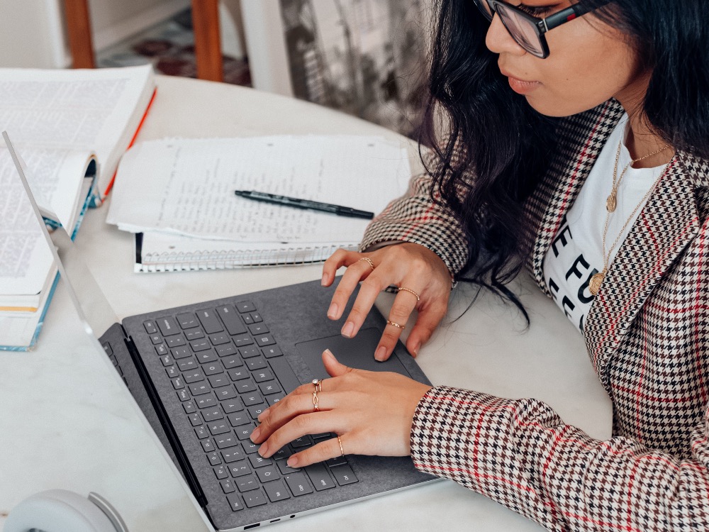 Student writing on a laptop with notes and a textbook