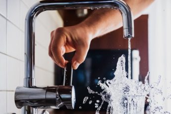 Person filling a water glass from a faucet