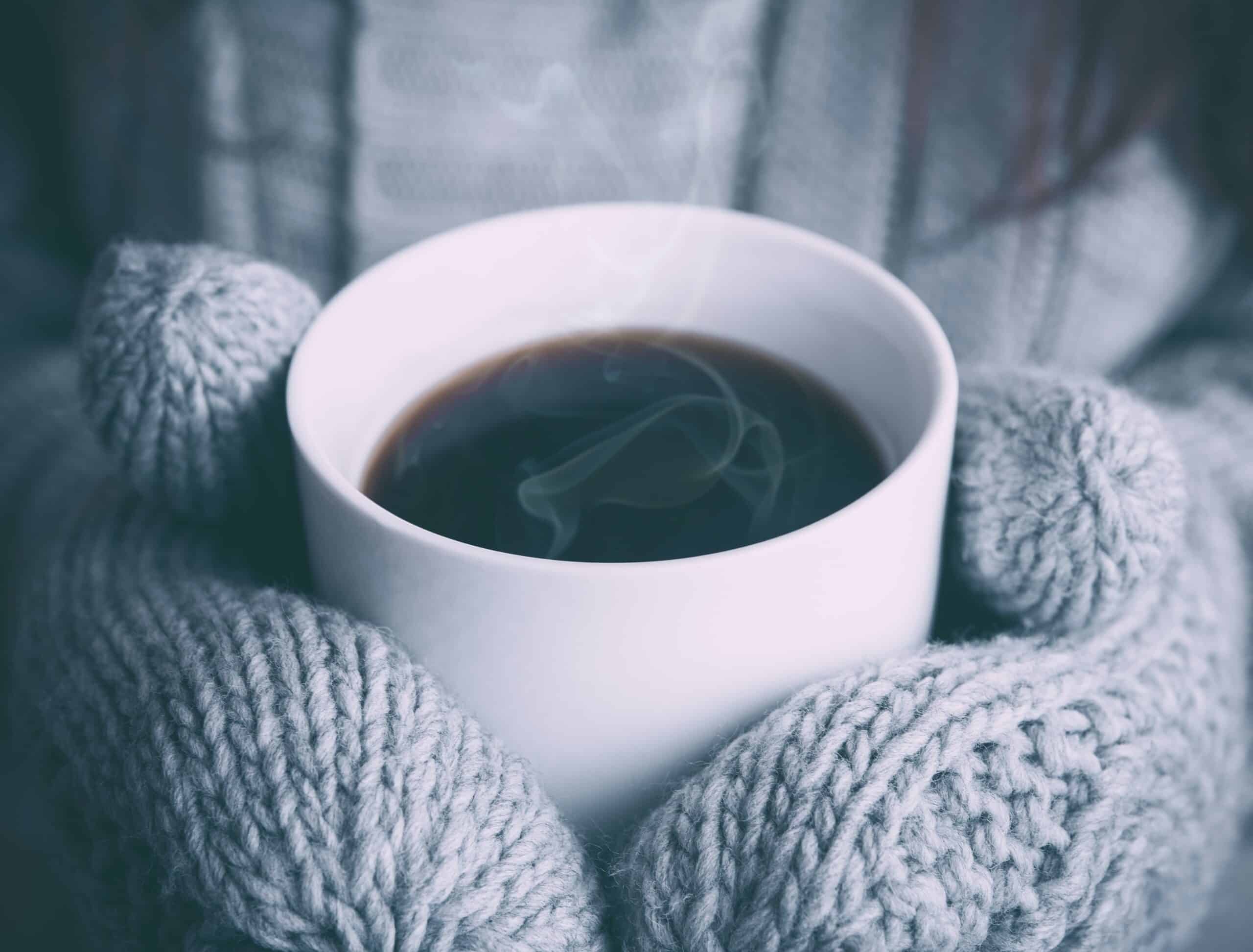 Two mitten hands holding a steaming cup of coffee