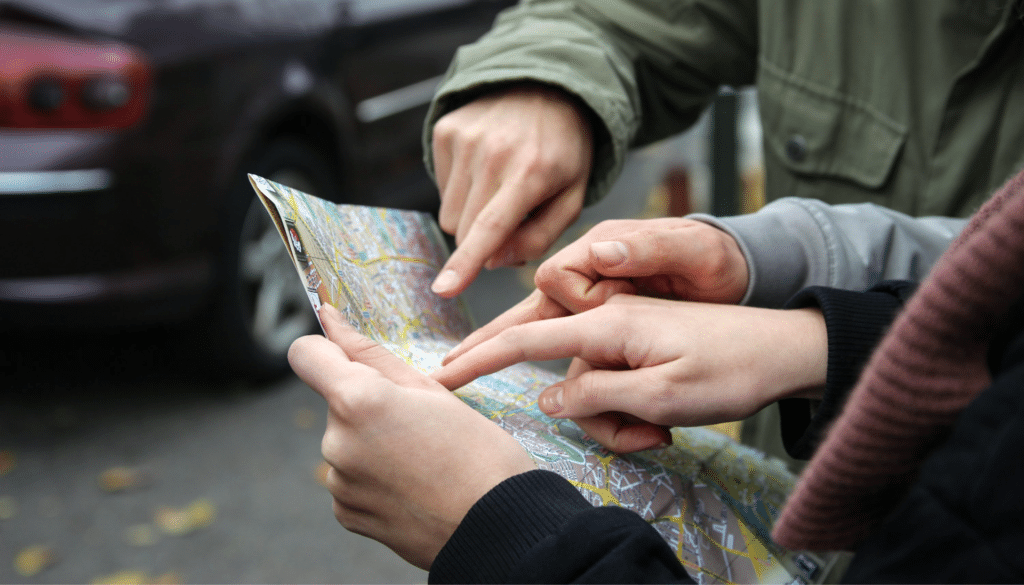 Two people pointing at a paper city map outdoors while planning a route, a hands-on way to practice geography and map skills